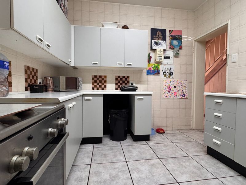 Functional kitchen featuring built-in cabinetry, tiled splashbacks, and tiled flooring, offering a practical layout with a freestanding oven and hob.
