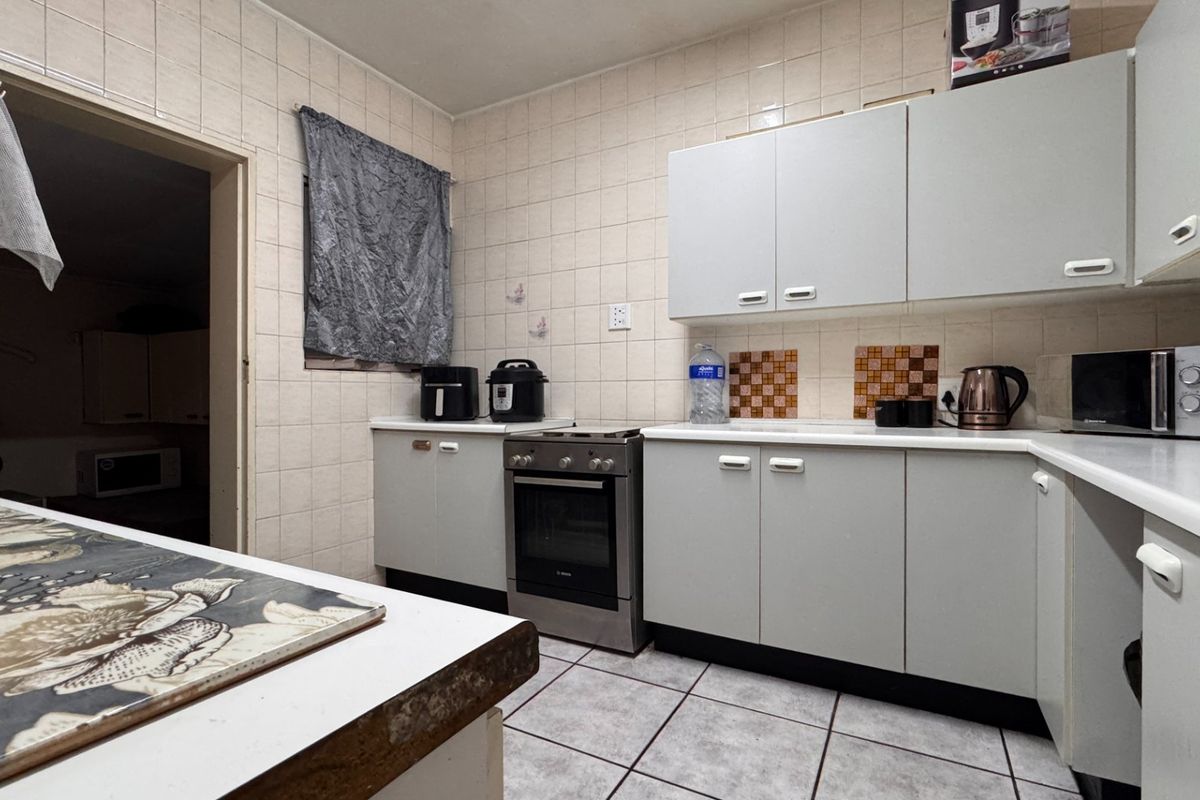A functional kitchen featuring tiled walls and flooring, built-in cabinetry, and a freestanding oven, offering a dated but practical layout.
