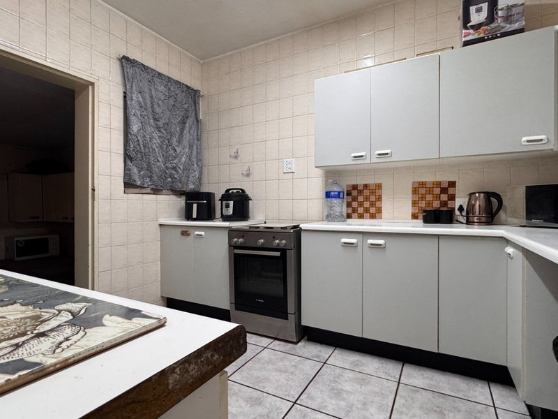 A functional kitchen featuring tiled walls and flooring, built-in cabinetry, and a freestanding oven, offering a dated but practical layout.