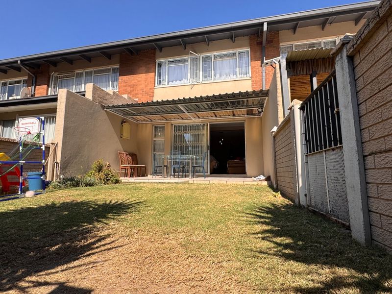 Rear view of the townhouse featuring a small private garden, a covered patio area, and a sliding door entrance.