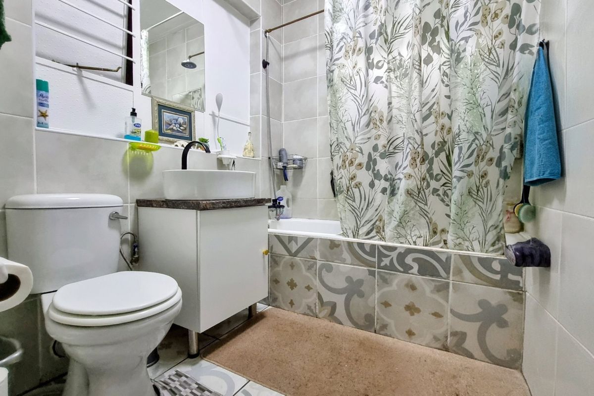 A compact bathroom featuring a vessel sink vanity, a standard toilet, and a bathtub with a tiled surround and shower curtain.