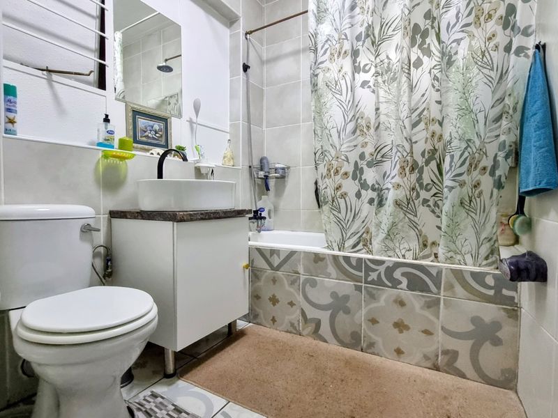 A compact bathroom featuring a vessel sink vanity, a standard toilet, and a bathtub with a tiled surround and shower curtain.