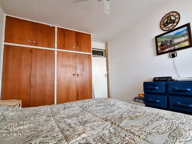 A bedroom featuring wooden built-in cupboards and a ceiling fan, offering functional storage space within the apartment.