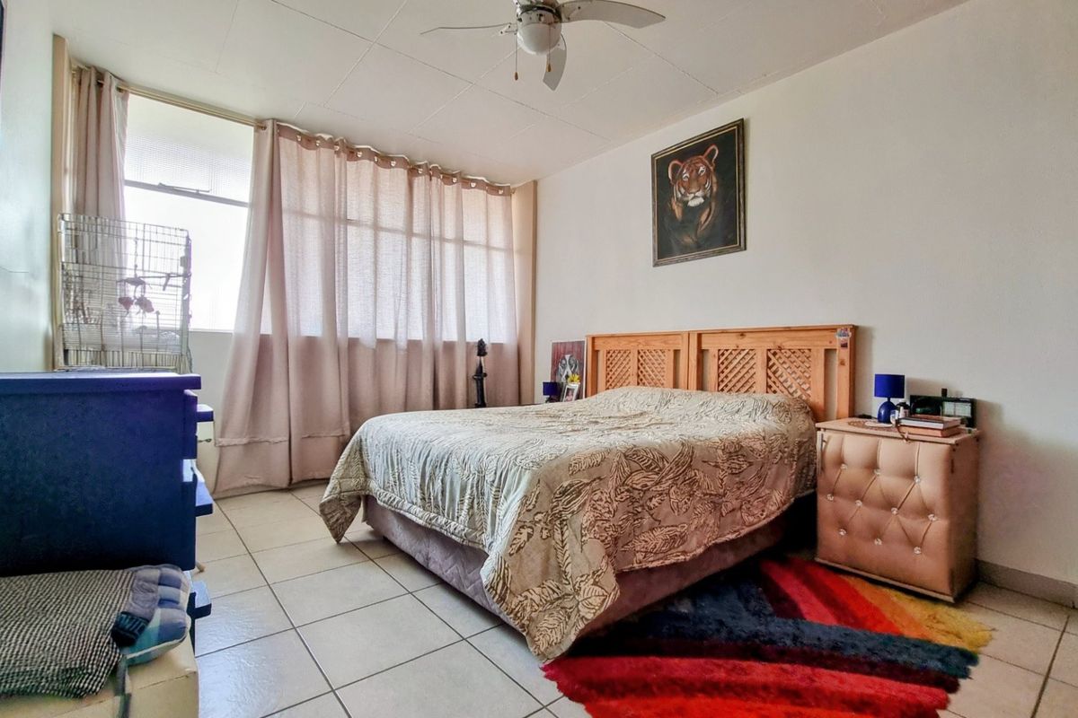 A spacious bedroom featuring tiled flooring, a ceiling fan, and a large window that allows for ample natural light.