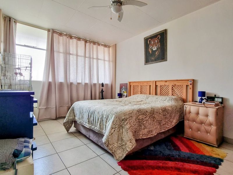 A spacious bedroom featuring tiled flooring, a ceiling fan, and a large window that allows for ample natural light.