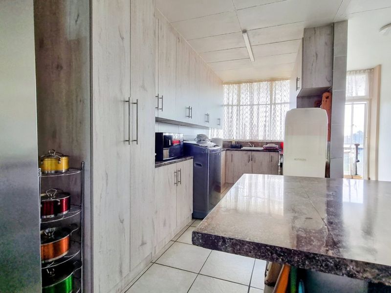 A functional kitchen featuring light wood-grain cabinetry, stone countertops, tiled flooring, and a double sink with ample storage space.