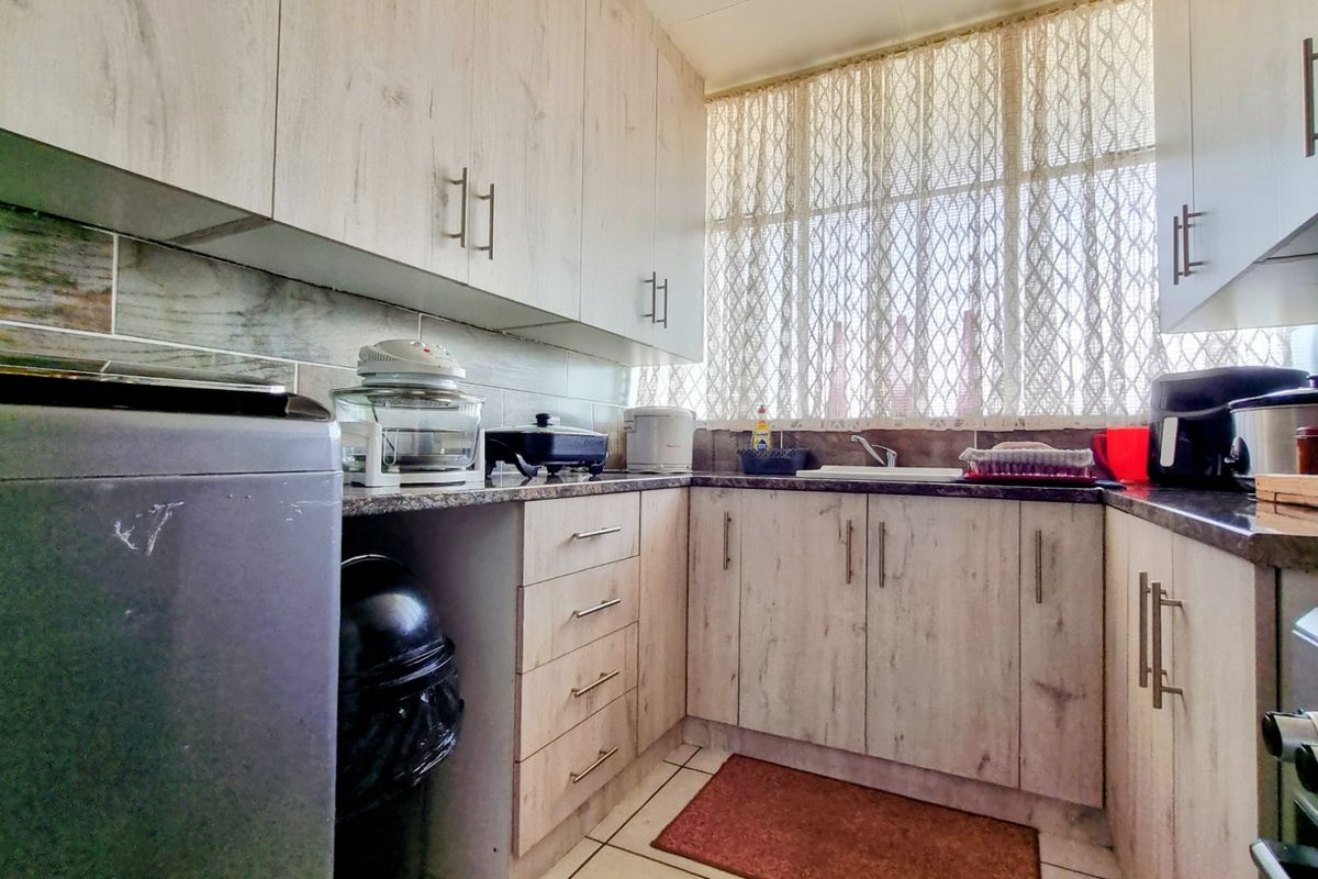 A functional kitchen featuring light wood-grain laminate cabinetry, granite countertops, a tiled backsplash, and a stainless steel sink with natural light.