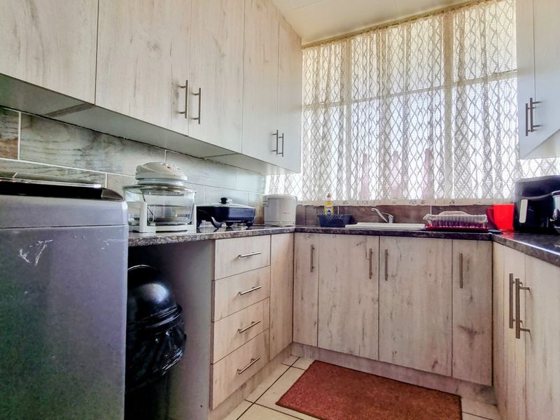 A functional kitchen featuring light wood-grain laminate cabinetry, granite countertops, a tiled backsplash, and a stainless steel sink with natural light.