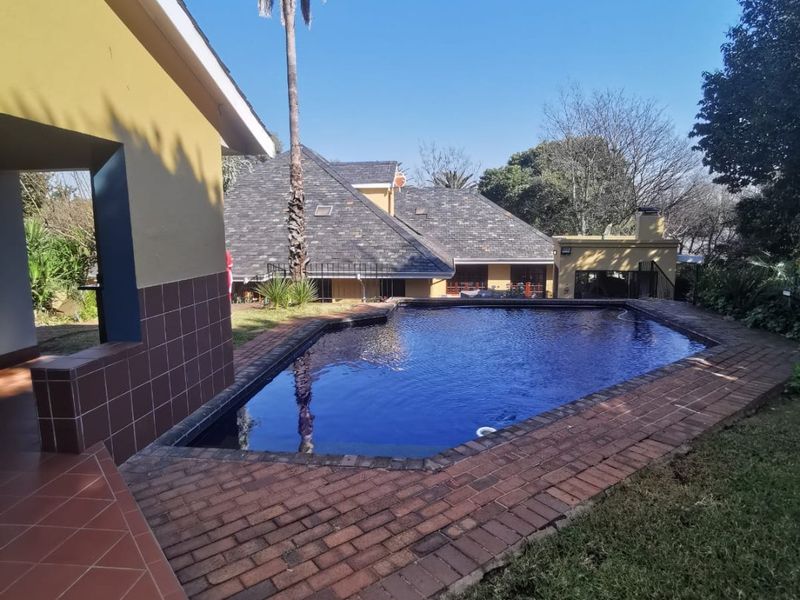 Outdoor entertainment area featuring a swimming pool with brick paving, a covered tiled patio, and an integrated outdoor fireplace.