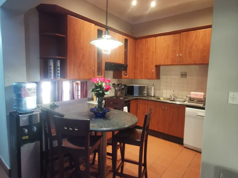 A functional kitchen featuring warm-toned wooden cabinetry, granite countertops, tiled flooring, and an integrated breakfast bar area with pendant lighting.