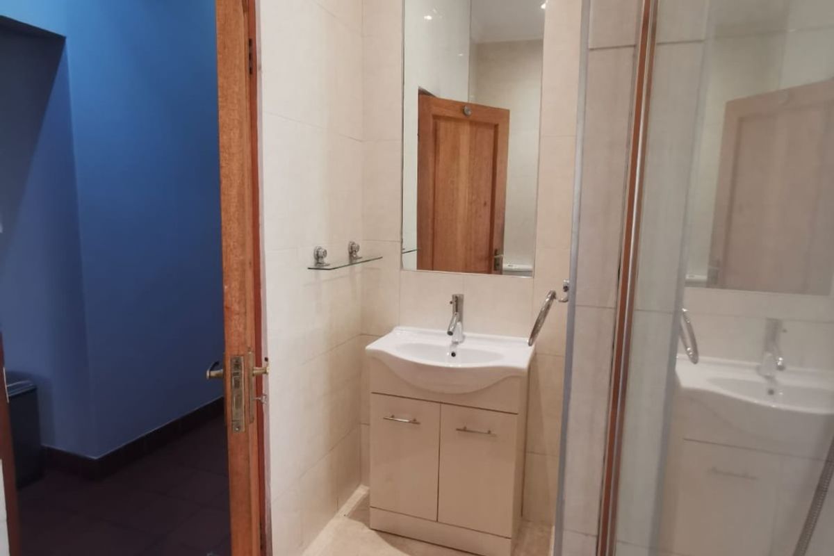 A clean, modern bathroom featuring a vanity basin, wall-mounted mirror, and a glass-enclosed shower with neutral tiled finishes.