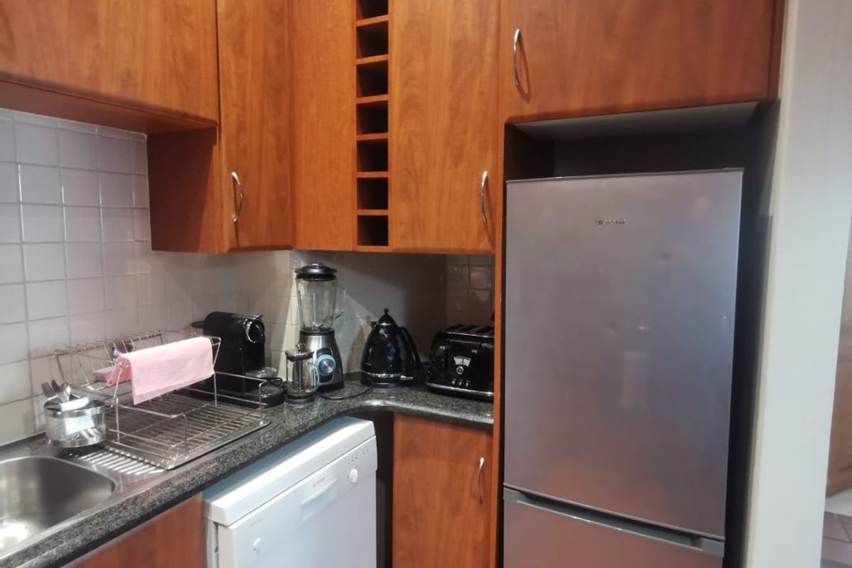 A functional kitchen featuring warm-toned laminate cabinetry, granite countertops, a tiled backsplash, and durable terracotta flooring with integrated storage solutions.