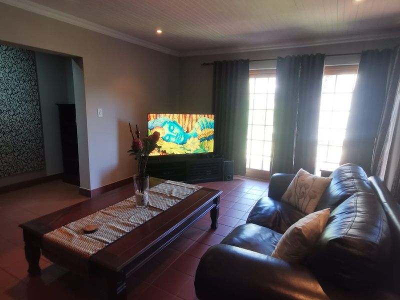 A comfortable living room featuring tiled flooring, a timber panelled ceiling with recessed lighting, and direct access to the outdoors through french doors.