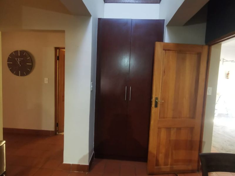 A hallway featuring terracotta floor tiles, a built-in dark wood cupboard, and a central skylight providing natural overhead illumination.