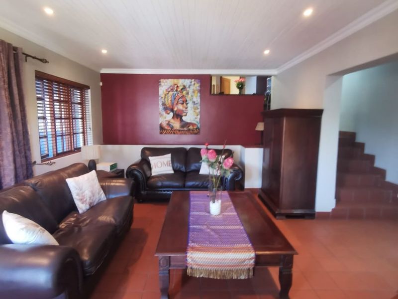 Spacious living room featuring terracotta floor tiles, a timber-look ceiling with recessed lighting, and an adjacent staircase leading to the upper level.