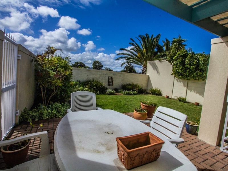 A covered patio area featuring brick paving, overlooking a private garden enclosed by boundary walls.