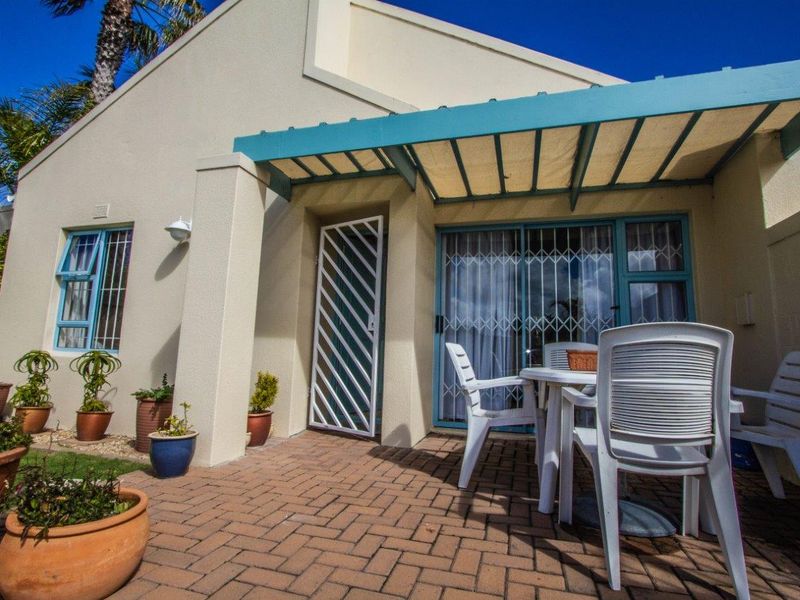 A paved outdoor patio area featuring a covered awning, sliding glass doors with security gates, and exterior wall lighting.