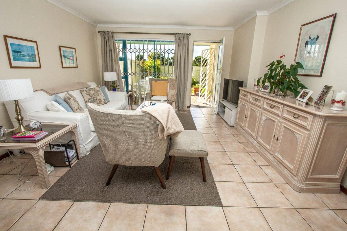 A bright living room featuring neutral tiled flooring and direct access to an outdoor patio area through a sliding glass door with security gate.