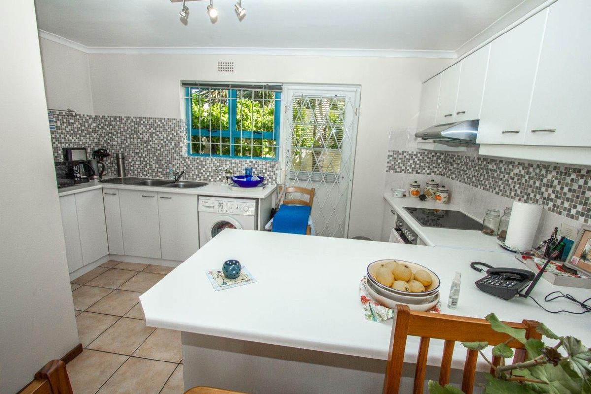 Functional kitchen featuring white cabinetry, tiled backsplash, integrated appliances, and direct access to the exterior through a security-fitted door.