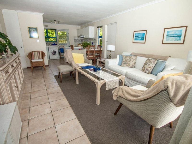 Open-plan living and kitchen area featuring tiled and carpeted flooring, functional cabinetry, and natural light through security-barred windows.