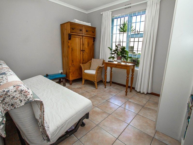 A bedroom featuring tiled flooring, a window with security bars, and a built-in cupboard, offering a functional and neutral living space.