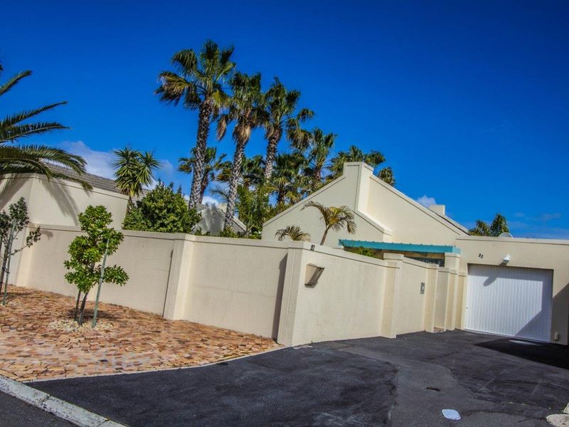 Front elevation of a residential property featuring a secure boundary wall, paved driveway, and a single garage door under a clear blue sky.