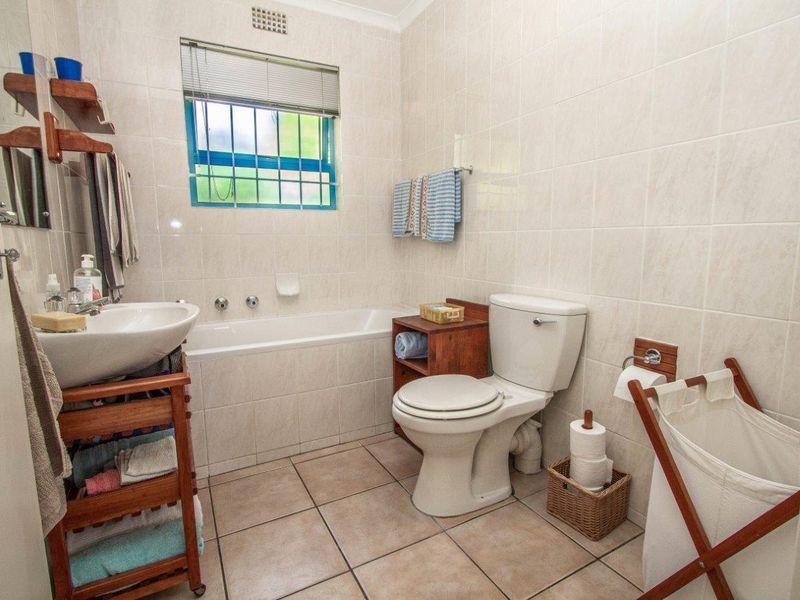 A functional bathroom featuring a built-in bathtub, toilet, and neutral ceramic tiling throughout, complete with a window for natural light and ventilation.