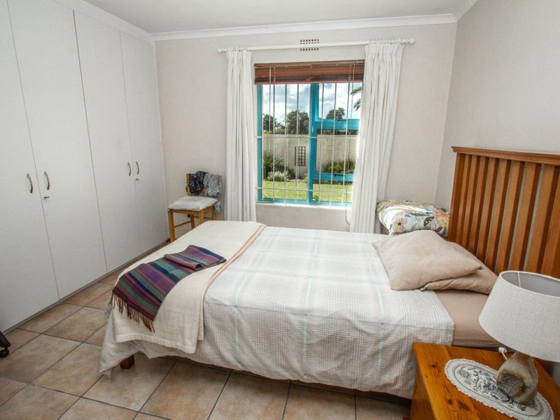 A functional bedroom featuring built-in cupboards, tiled flooring, and a window with security bars overlooking the garden.