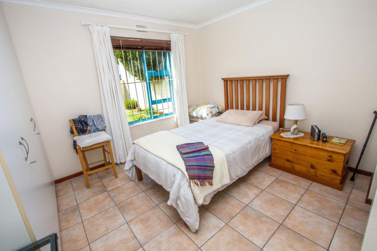 A functional bedroom featuring tiled flooring, a built-in wardrobe, and security bars on the window, providing a practical and secure living space.