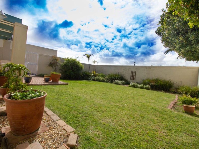 A private rear garden featuring a well-maintained lawn, a paved patio area, and high boundary walls for added privacy.