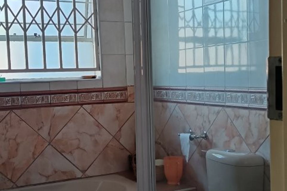 A functional bathroom featuring a built-in bathtub, separate shower enclosure, and toilet, finished with decorative wall and floor tiling.