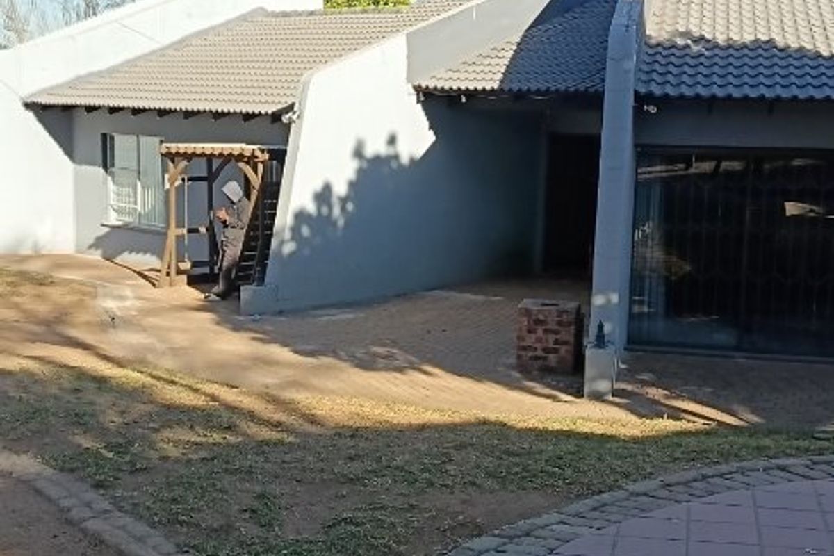 Rear exterior view of the commercial property featuring a paved patio area, brick built-in braai, and sliding glass door access.