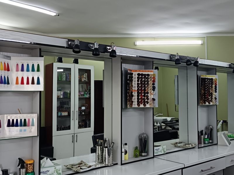 A commercial salon space featuring multiple built-in workstations with integrated mirrors, overhead fluorescent lighting, and ample storage cabinetry.