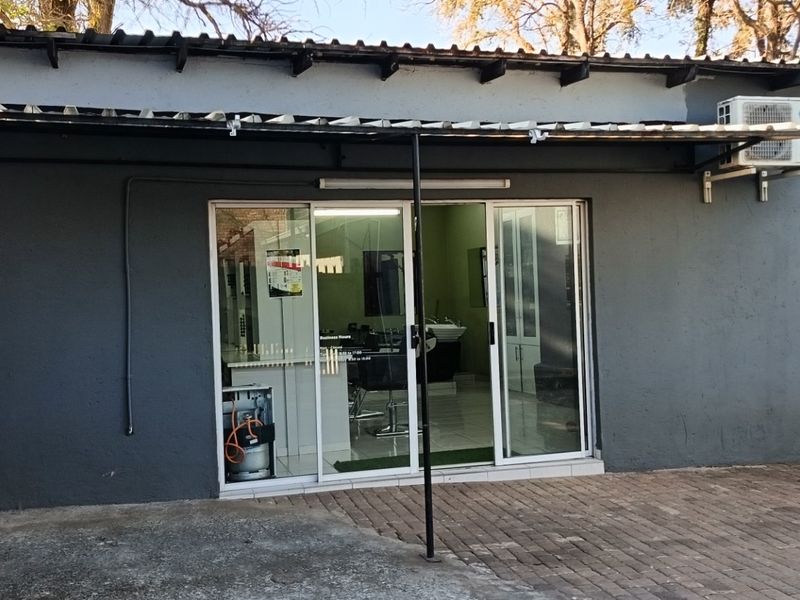 Rear exterior view of a commercial property featuring a paved patio area, sliding glass entrance, and wall-mounted air conditioning unit.