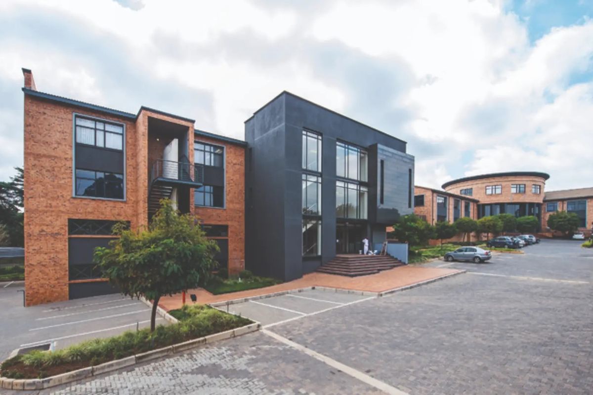 A modern commercial office complex featuring a combination of exposed brick and dark contemporary facade elements with an expansive paved parking area.