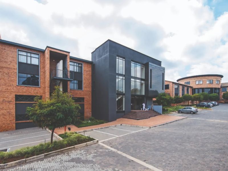 A modern commercial office complex featuring a combination of exposed brick and dark contemporary facade elements with an expansive paved parking area.