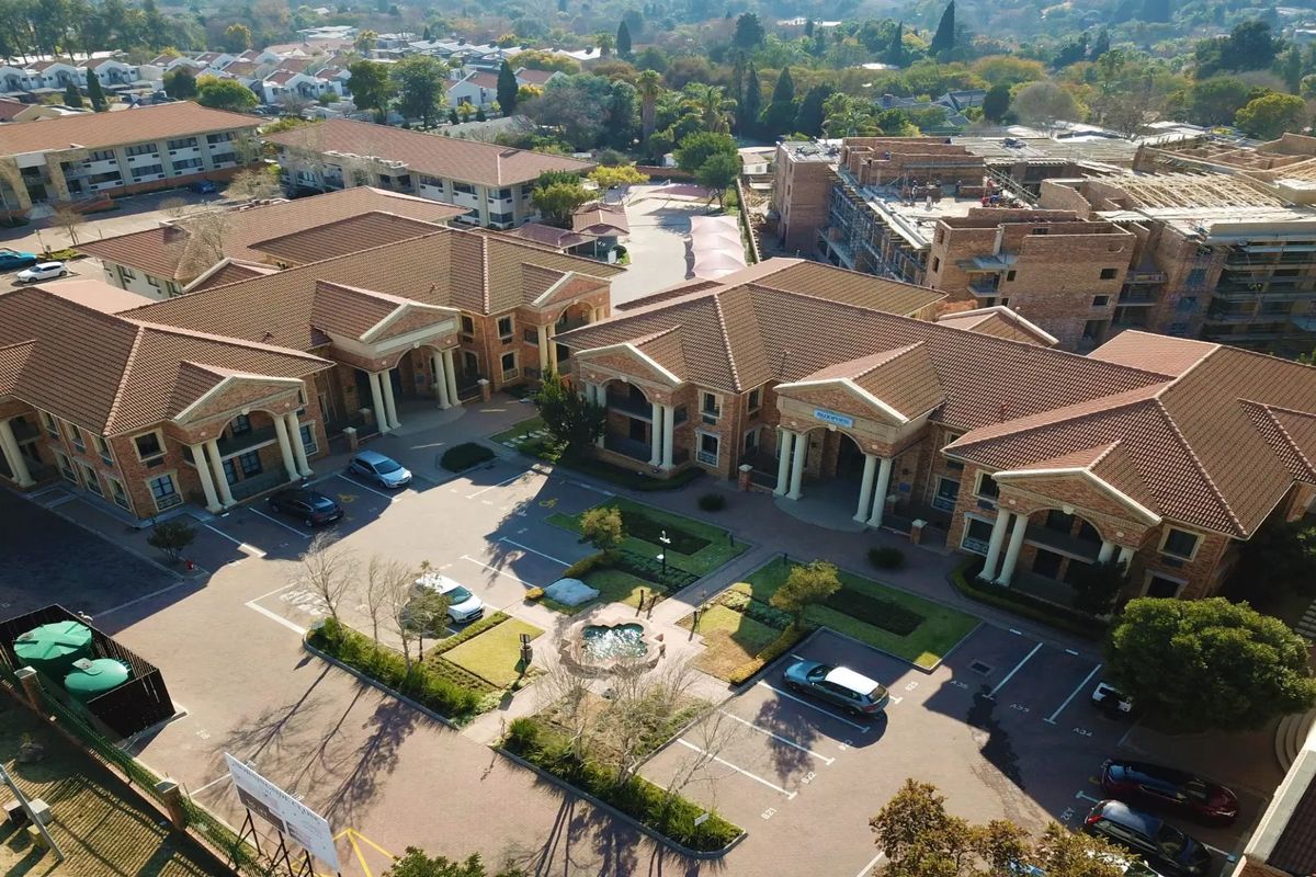 Aerial view of a commercial office complex featuring multiple brick buildings with tiled roofs, paved parking, landscaped gardens, and a central water fountain.