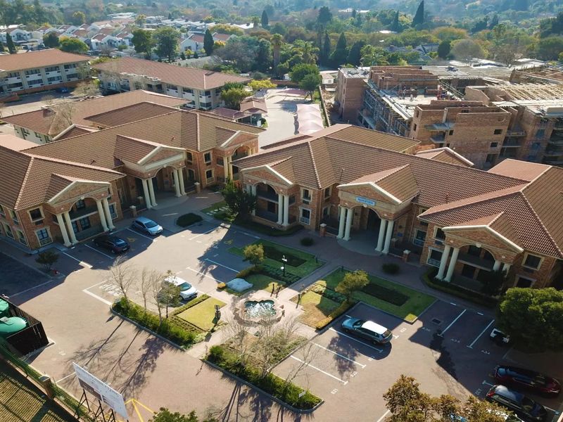 Aerial view of a commercial office complex featuring multiple brick buildings with tiled roofs, paved parking, landscaped gardens, and a central water fountain.