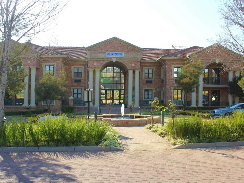 Front elevation of a commercial office building featuring a brick facade, classical columns, a central fountain, and well-maintained landscaped gardens.