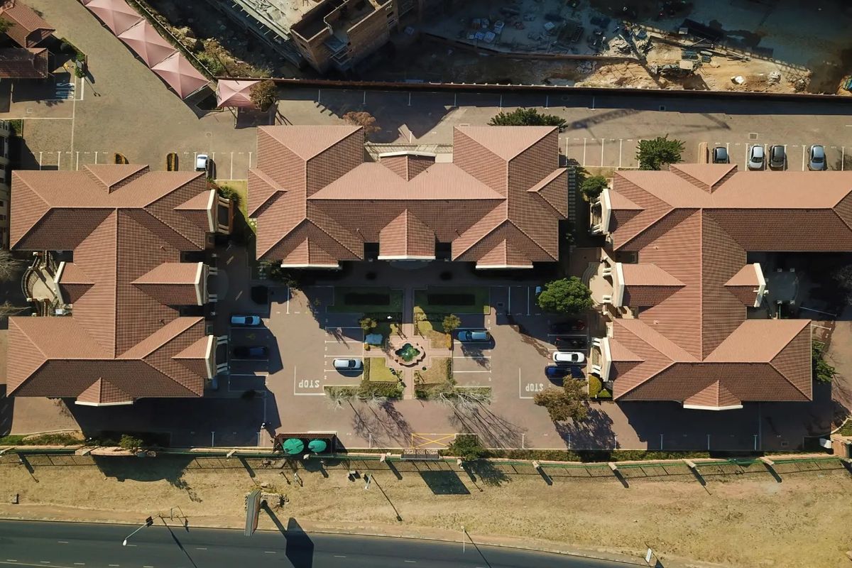 Aerial view of a commercial office complex featuring multiple buildings with tiled roofs, central courtyard, and extensive paved parking facilities.
