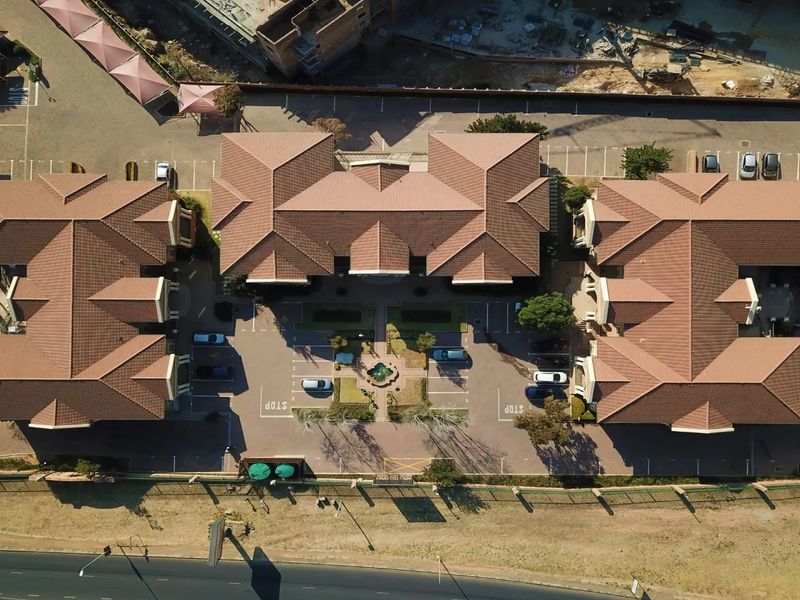 Aerial view of a commercial office complex featuring multiple buildings with tiled roofs, central courtyard, and extensive paved parking facilities.