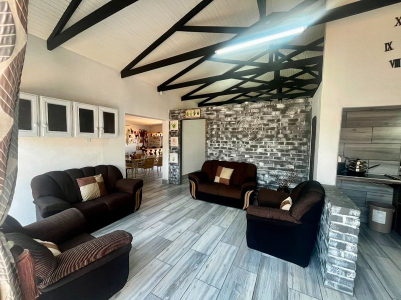 Spacious open-plan living area featuring a vaulted ceiling with exposed trusses, a rustic brick feature wall, and modern tiled flooring.