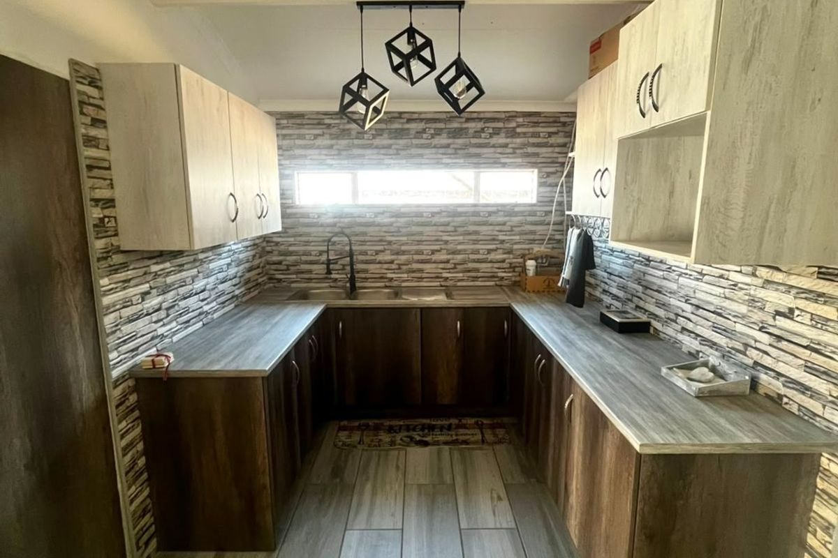 A modern kitchen featuring dark wood-tone cabinetry, light wood-effect countertops, a tiled backsplash, and contemporary pendant lighting.