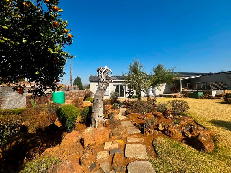 A spacious rear garden featuring a stone pathway, established landscaping, and a covered patio area attached to the main residence.