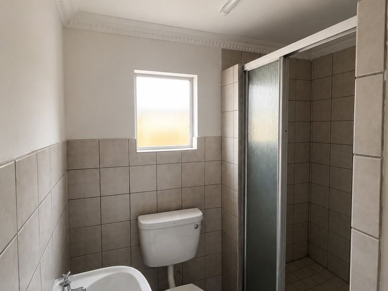 A functional bathroom featuring a shower enclosure, pedestal basin, and toilet with neutral wall tiling and classic cornice detailing.