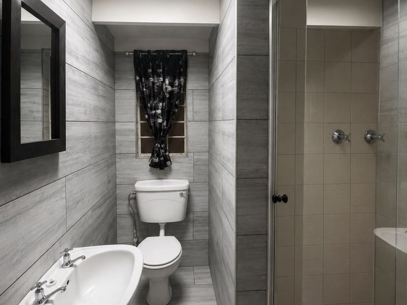 Modern bathroom featuring grey wood-look wall and floor tiles, a pedestal basin, and a separate glass-enclosed shower area.