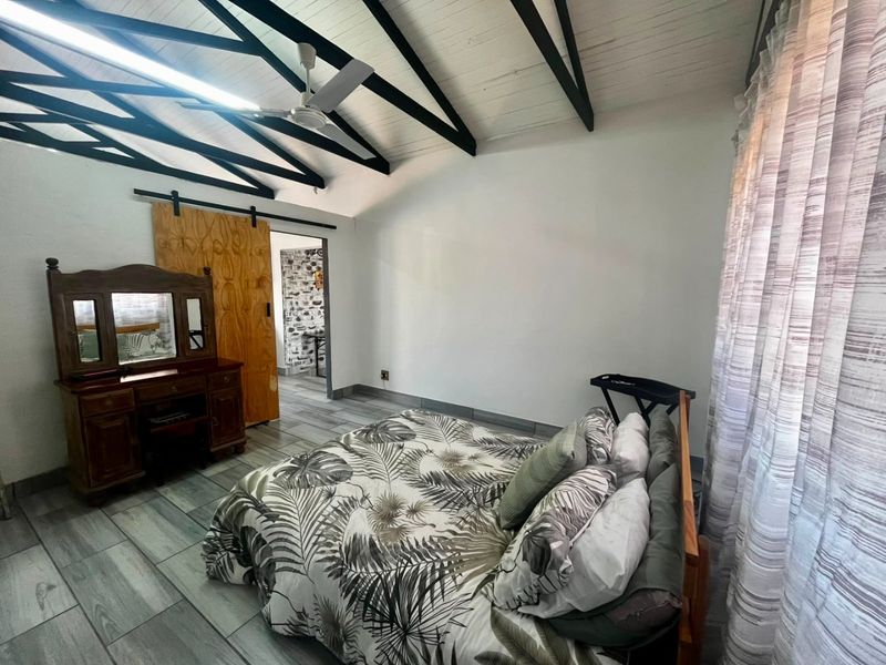 Spacious bedroom featuring a vaulted ceiling with exposed timber beams, tiled flooring, and a sliding barn door leading to an adjacent room.