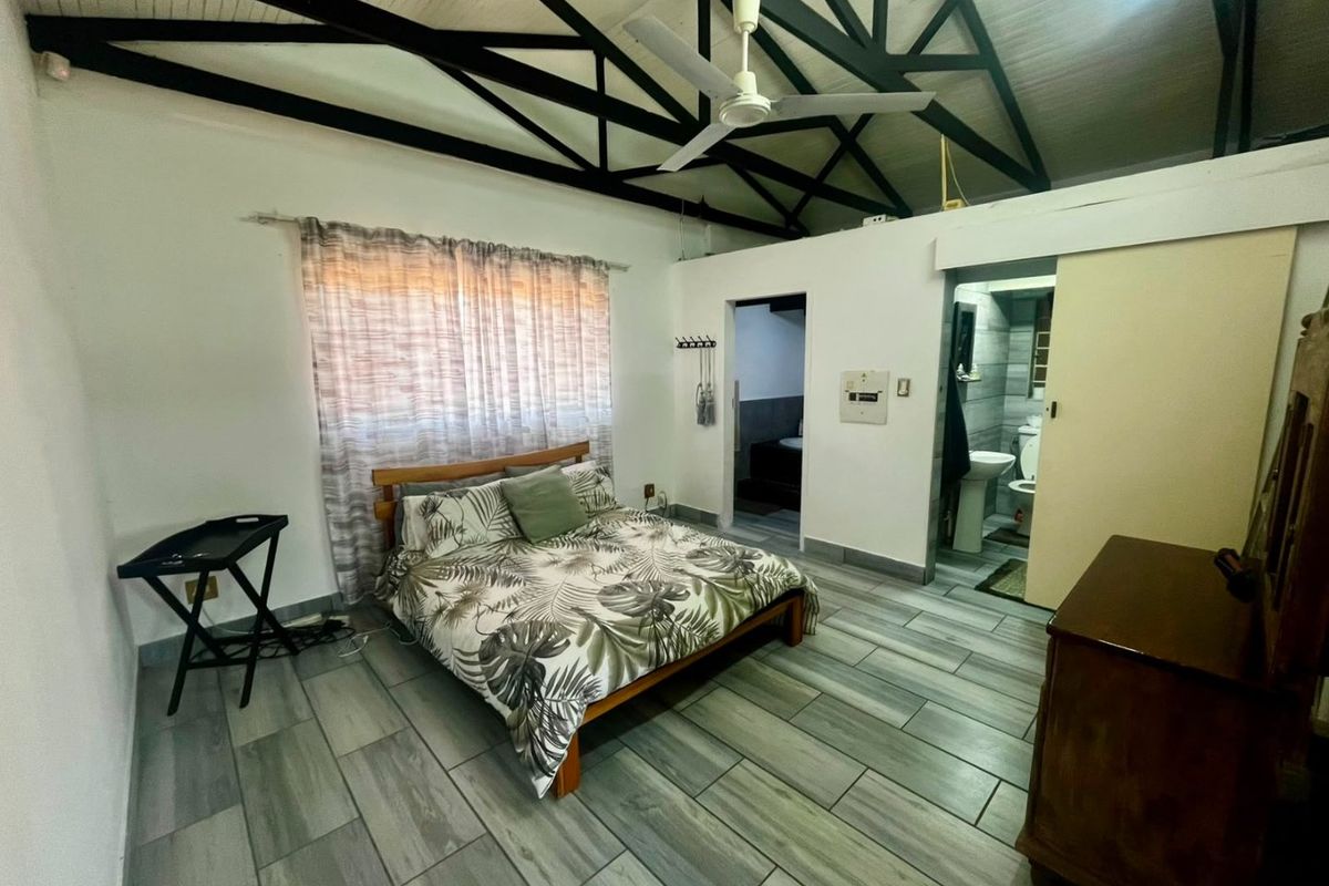 Spacious bedroom featuring exposed roof trusses, ceiling fan, modern tiled flooring, and direct access to an en-suite bathroom.