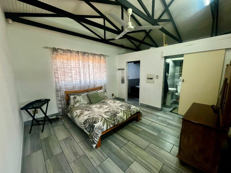 Spacious bedroom featuring exposed roof trusses, ceiling fan, modern tiled flooring, and direct access to an en-suite bathroom.