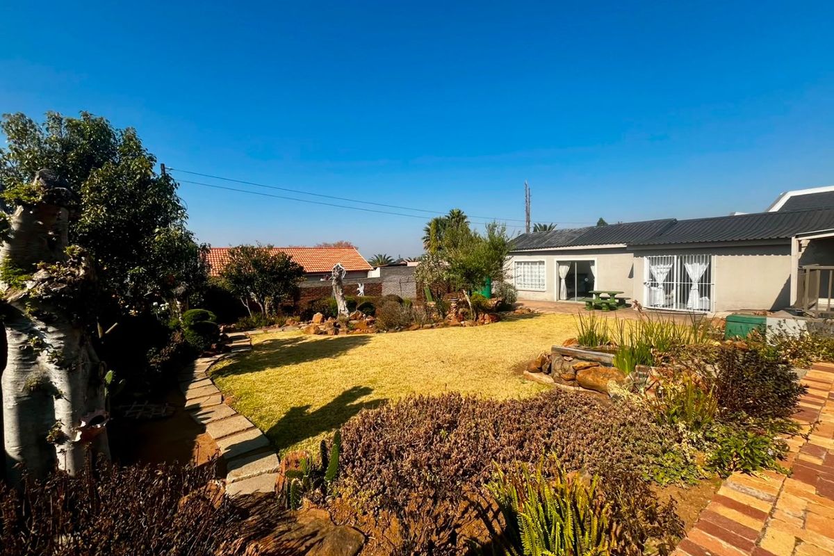 A well-maintained rear garden featuring a lawn, stone pathways, and established landscaping, providing access to the main dwelling via sliding glass doors.